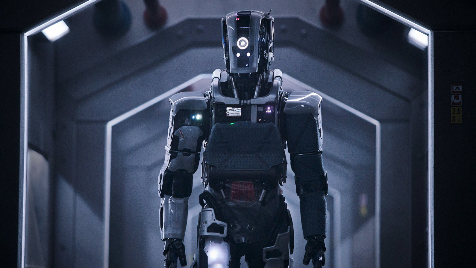 A director's silhouette against a giant LED screen showing a robot face mid-render, a busy VFX studio around him lit in cool blue, concept sketches pinned to the walls